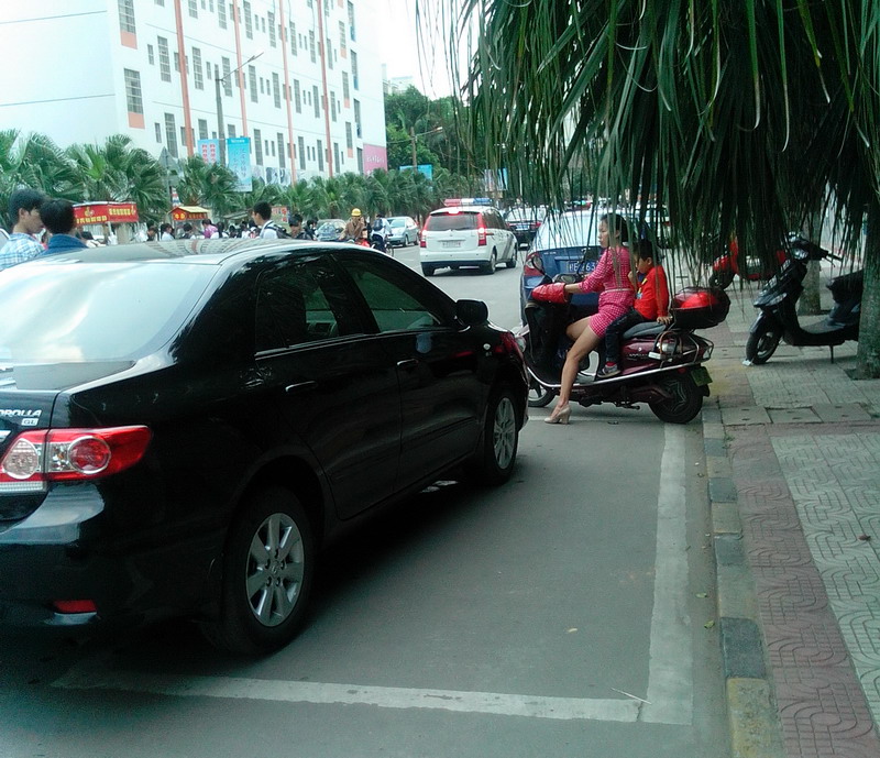 一个女人骑一辆电动车占着两个停车位中间,不